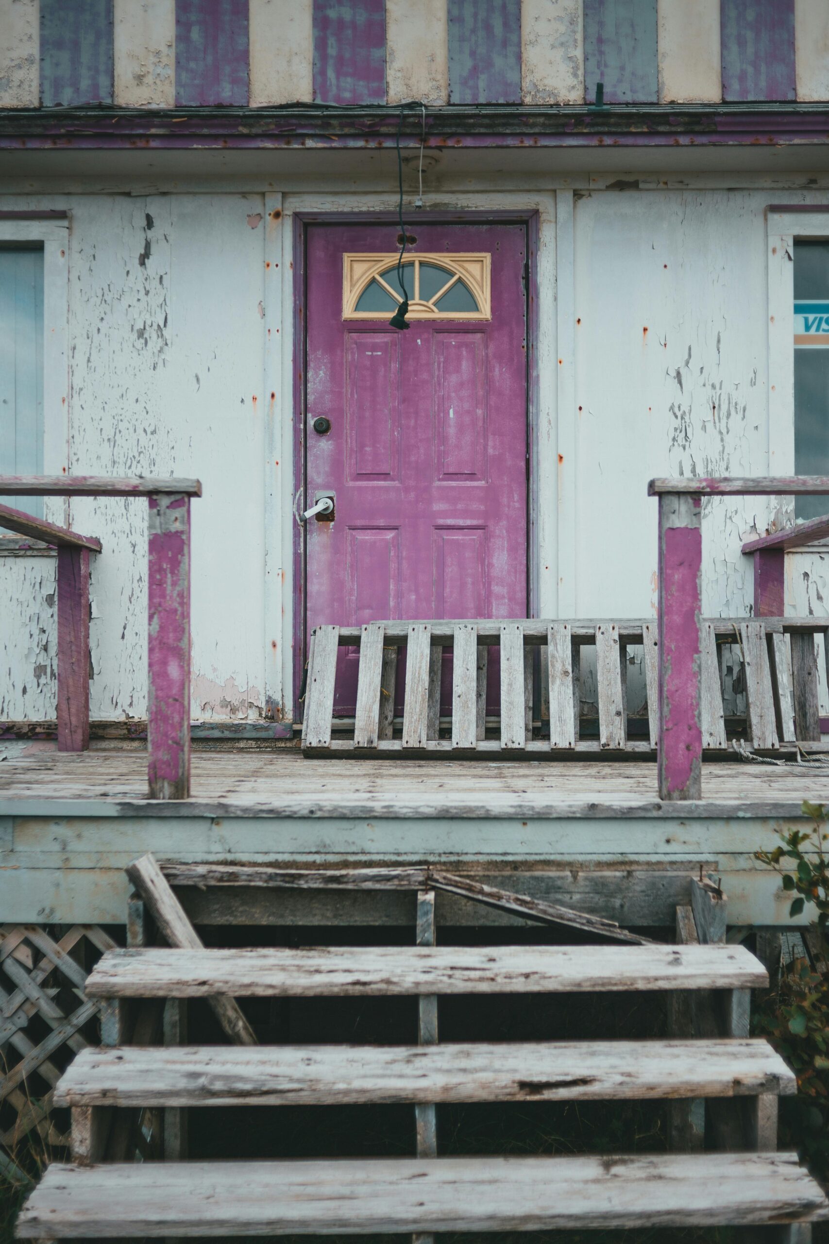 Weathered wooden porch with a vibrant purple door, showcasing rustic charm and abandonment.